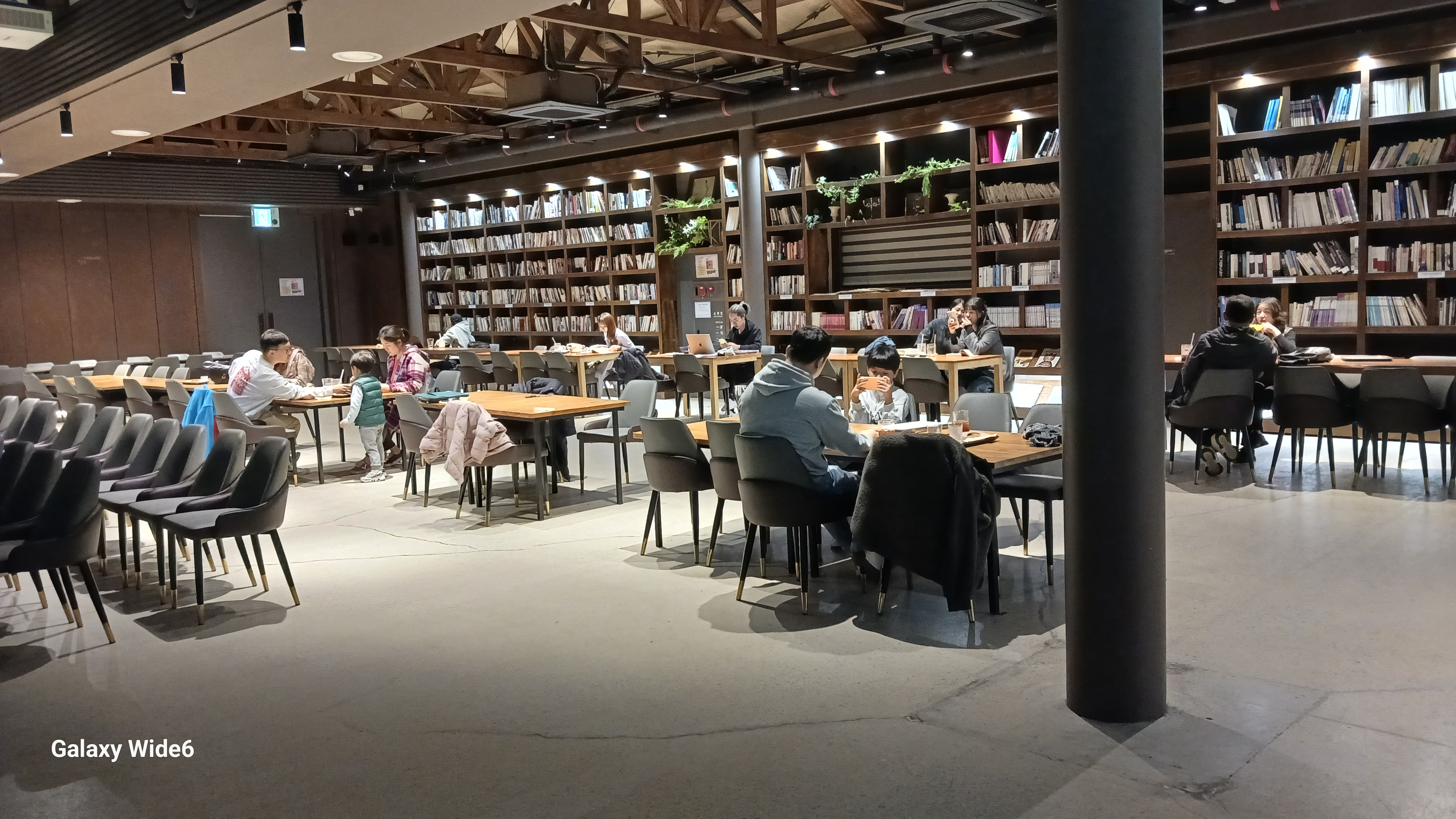 조치원 1927 아트센터 다목적홀에 책들이 진열되어 있고, 테이블 들에 사람들이 앉아있다.